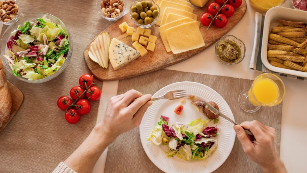 Overhead view of a cheese platter with fresh salad and juice, perfect for a gourmet lunch setting.